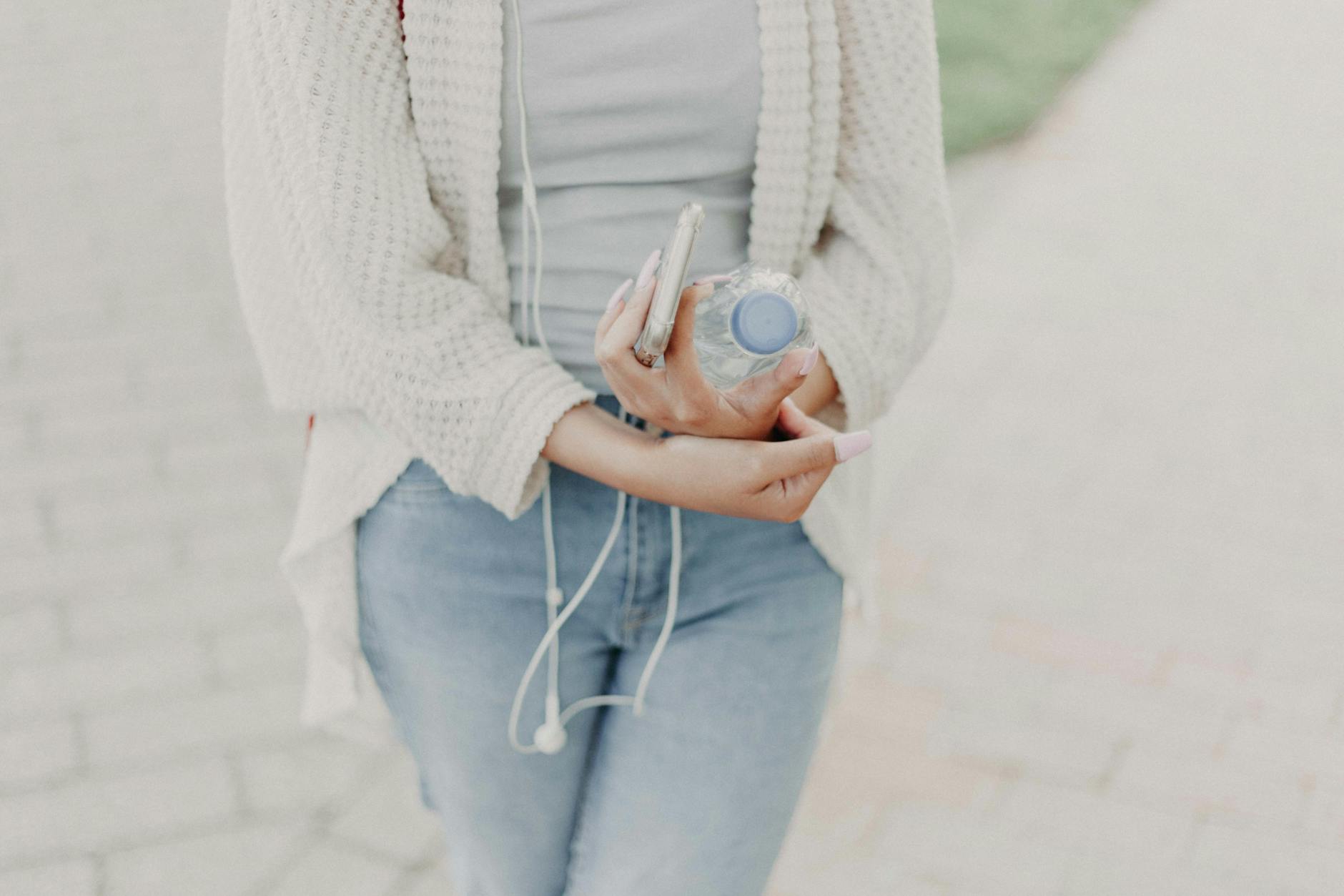 woman wearing white cardigan holding plastic bottle