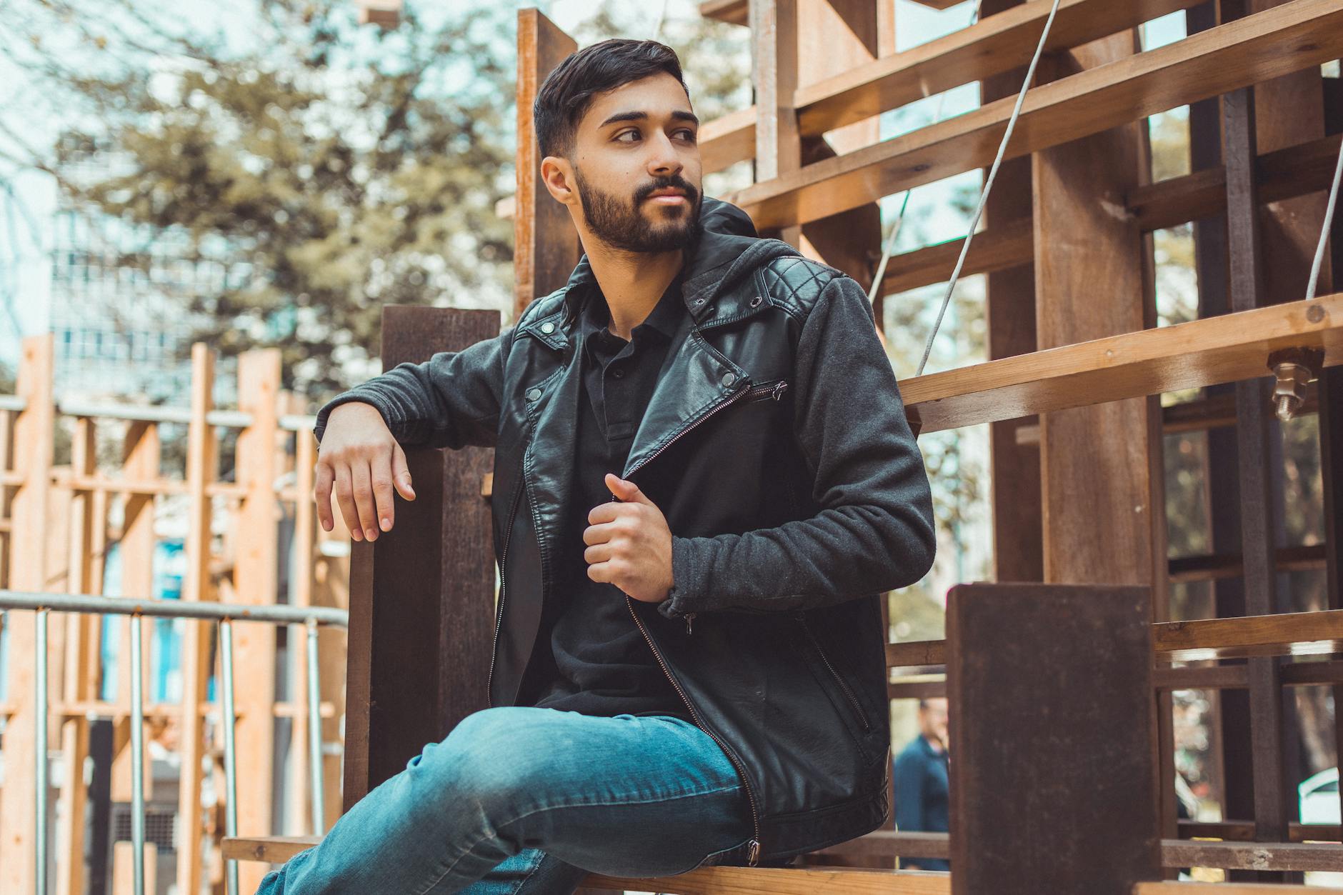 man wearing black jacket and jeans sitting on brown wooden chair
